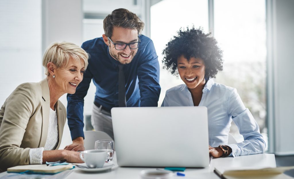 Three diverse business professionals collaborating and smiling while looking at a laptop screen during a meeting in a bright, modern office setting of BPT Australia